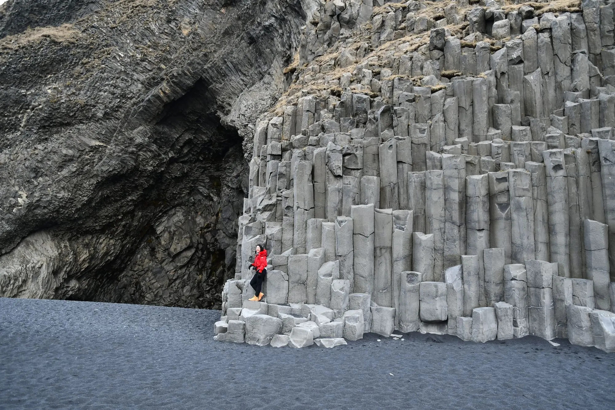 นักท่องเที่ยวยืนบนเสาหินบะซอลต์ริมหาดทรายดำ Reynisfjara