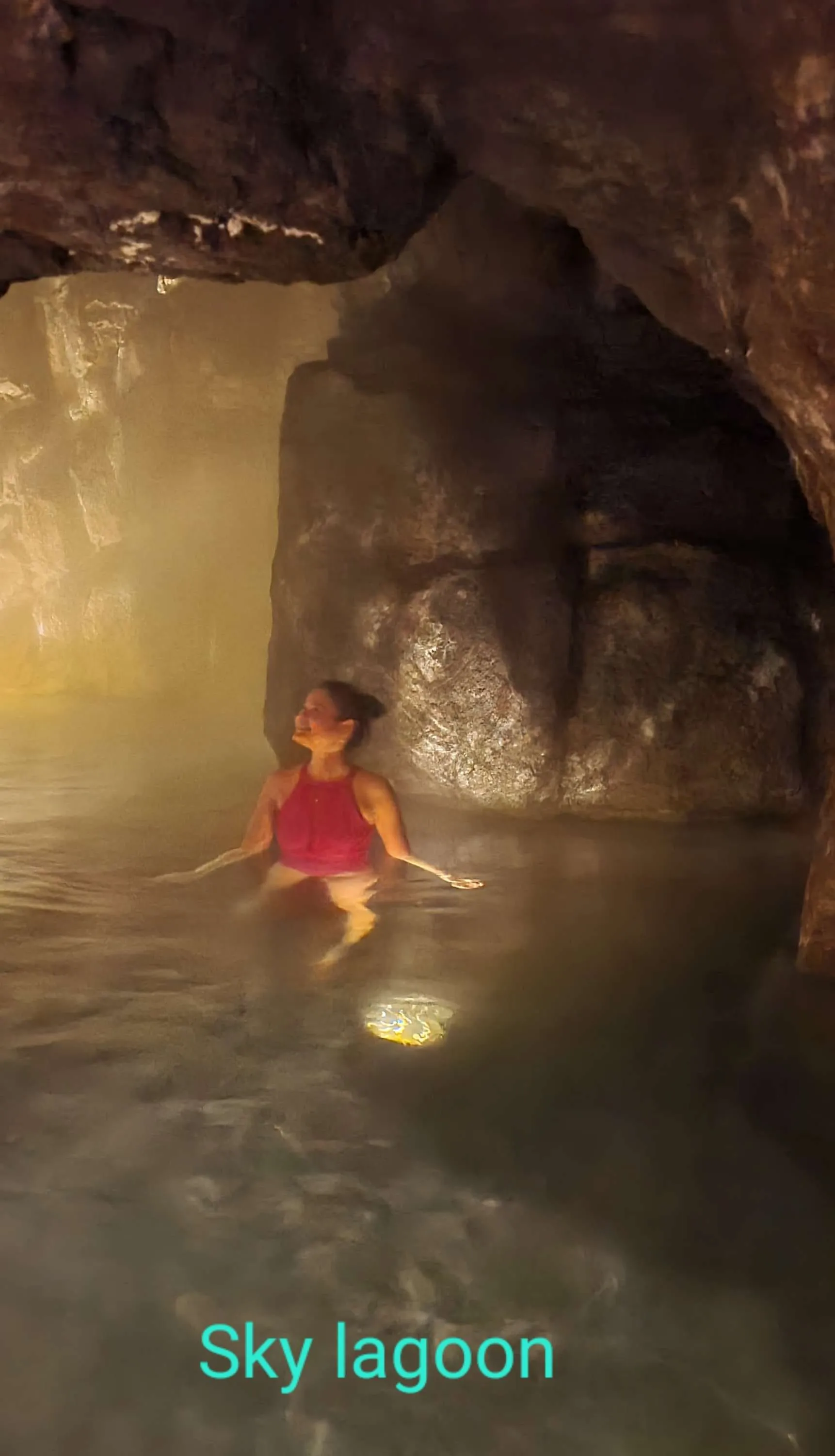 หญิงสาวนั่งแช่น้ำอุ่นข้างผนังหินใน Sky Lagoon