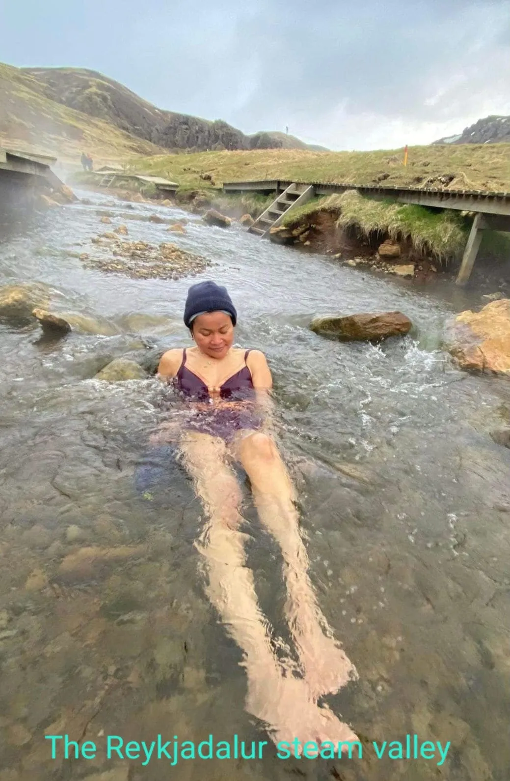 หญิงสาวนั่งแช่ในลำธารน้ำร้อนธรรมชาติที่หุบเขา Reykjadalur